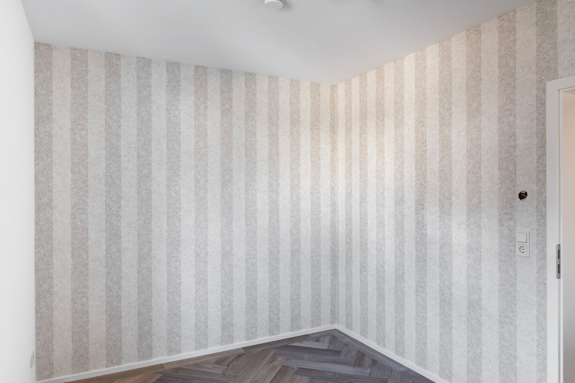 Ein Zimmer mit einer vertikal weiß-hellgrau gestreiften Tapete.
