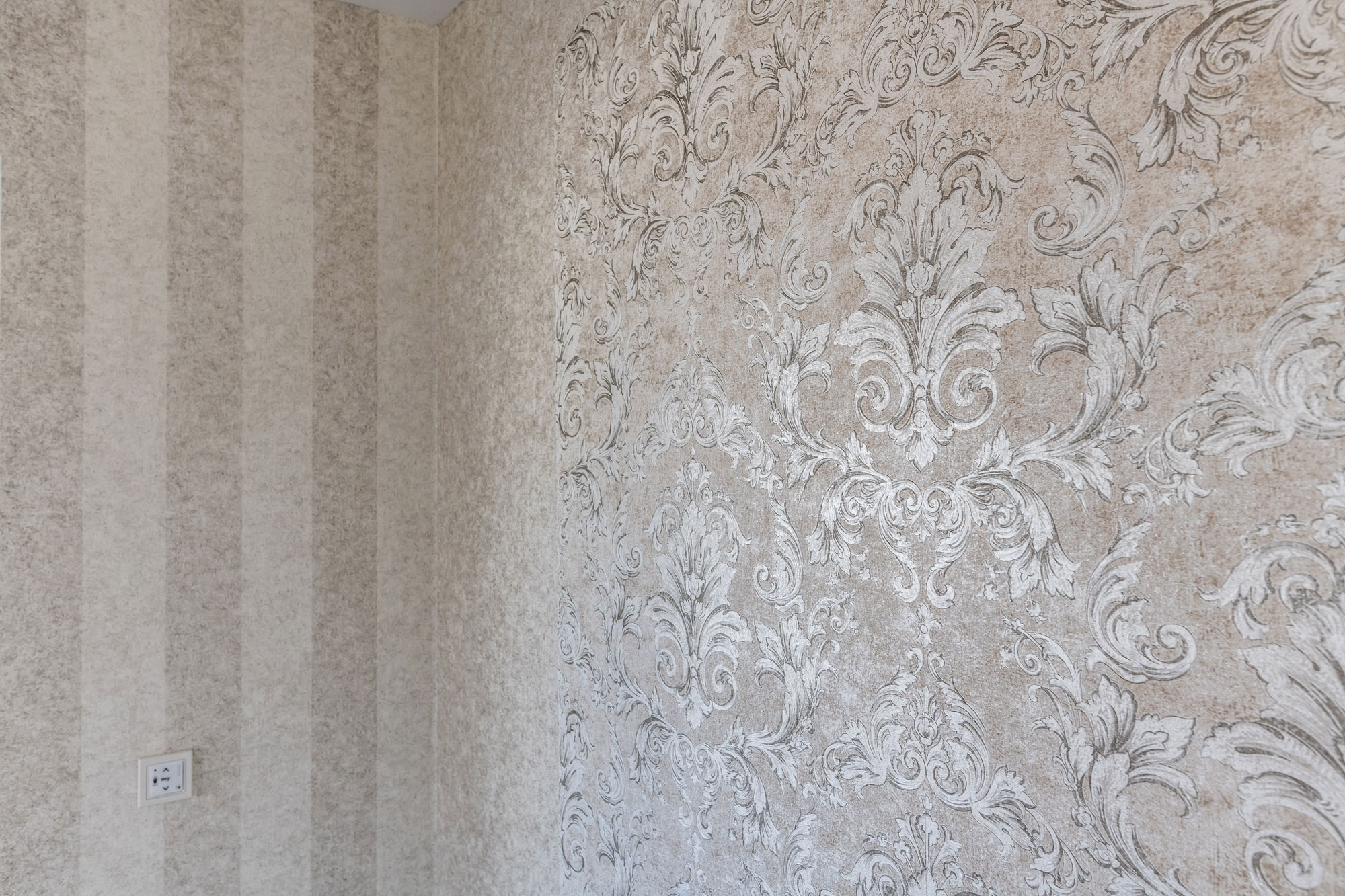 Klassische Ornamenttapete in weiß, silber und altrosa an einer Wohnzimmerwand.