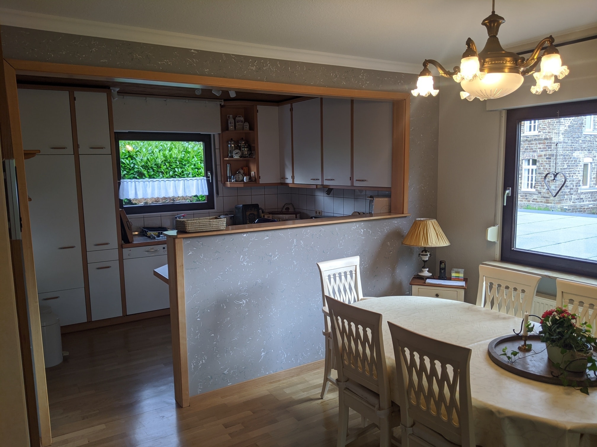 Eine biedere Wohnküche mit einer grau.weiß melierten Küchentheke und einem Esstisch mit weißen Holzstühlen.