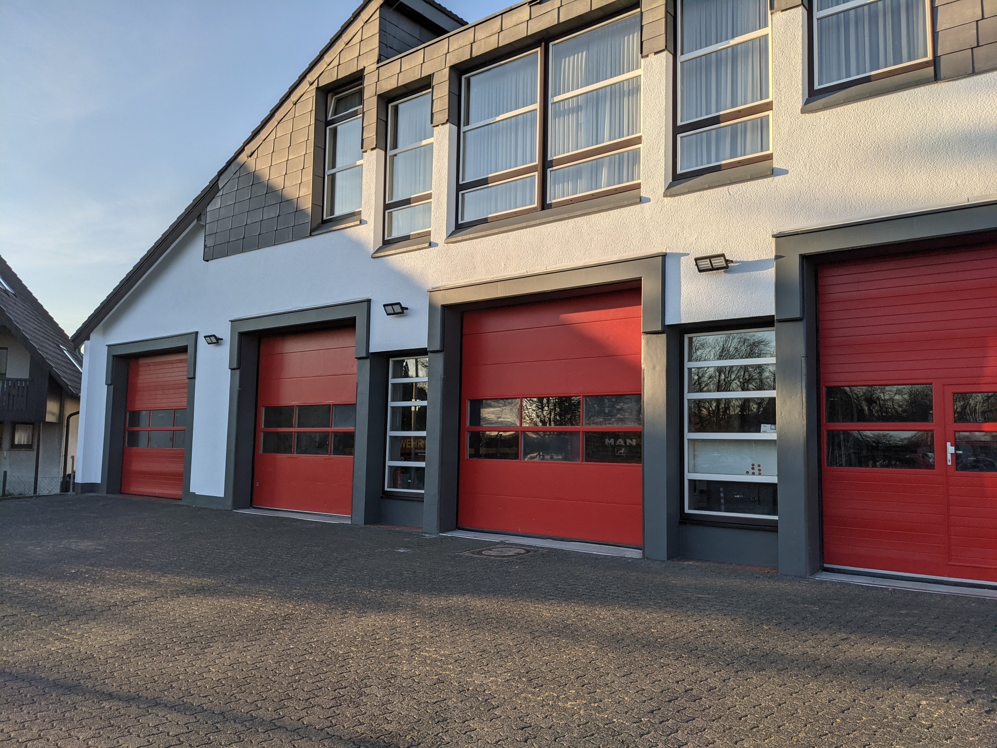 Die frisch gestrichene Fassade der Feuerwehr in Hennef an der Sieg mit roten Rolltoren in grau abgesetzt und weißer Fassade.