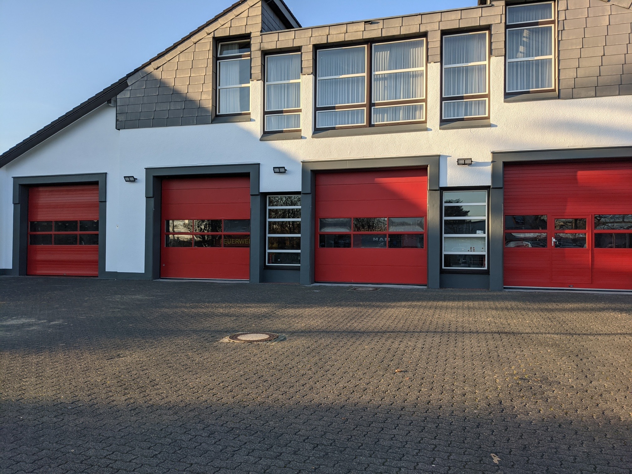 Fassade einer Feuerwehr mit roten Rolltoren ie grau abgesetzt sind und einer weißen Fassade.
