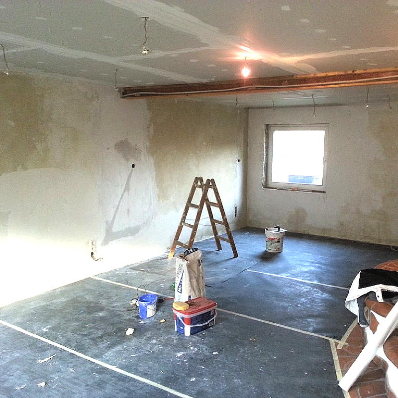 Ein leeres Zimmer beim Beginn von Malerarbeiten. In der Baustelle sind alle Wände sind gespachtelt und die Decke mit Rigipsplatten abgehangen, der Boden ist mit Malerflies abgeklebt.